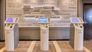 Three self-service kiosks in a hotel lobby with motivational phrases on the wall behind them. - Premier Inn Manchester Cc Princess Street (Manchester)
