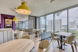A modern restaurant with high ceilings, large windows, and a view of the cityscape. - Premier Inn Manchester Cc Princess Street (Manchester)