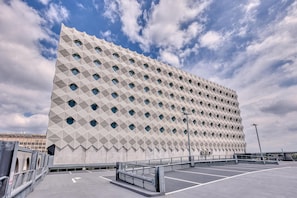 Egy modern épület, geometriai mintázatú homlokzattal és előtte egy parkolóval.