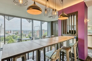 A modern dining area with a long wooden table, bar stools, and pendant lighting. - Premier Inn Manchester Cc Princess Street (Manchester)