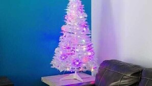 Una sala de estar con pared azul, un sofá de cuero negro y un árbol de Navidad blanco con luces moradas.