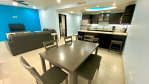 Una sala de estar moderna con un sofá, una mesa de comedor con sillas, una zona de cocina con un refrigerador y un televisor.