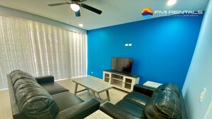 Una sala de estar moderna con una pared de acento azul, un televisor de pantalla plana y un ventilador de techo.