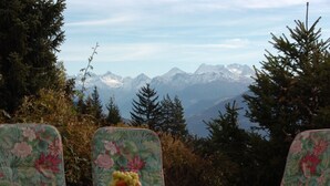 A table with a floral tablecloth and a bowl of fruit, set against a backdrop of mountains and trees.