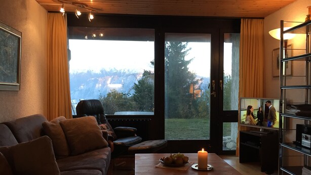A cozy living room with a couch, a coffee table with a candle, and a TV displaying a show.