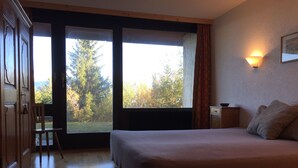 A bedroom with a large bed, a chair, a nightstand, and a window with a view of trees.