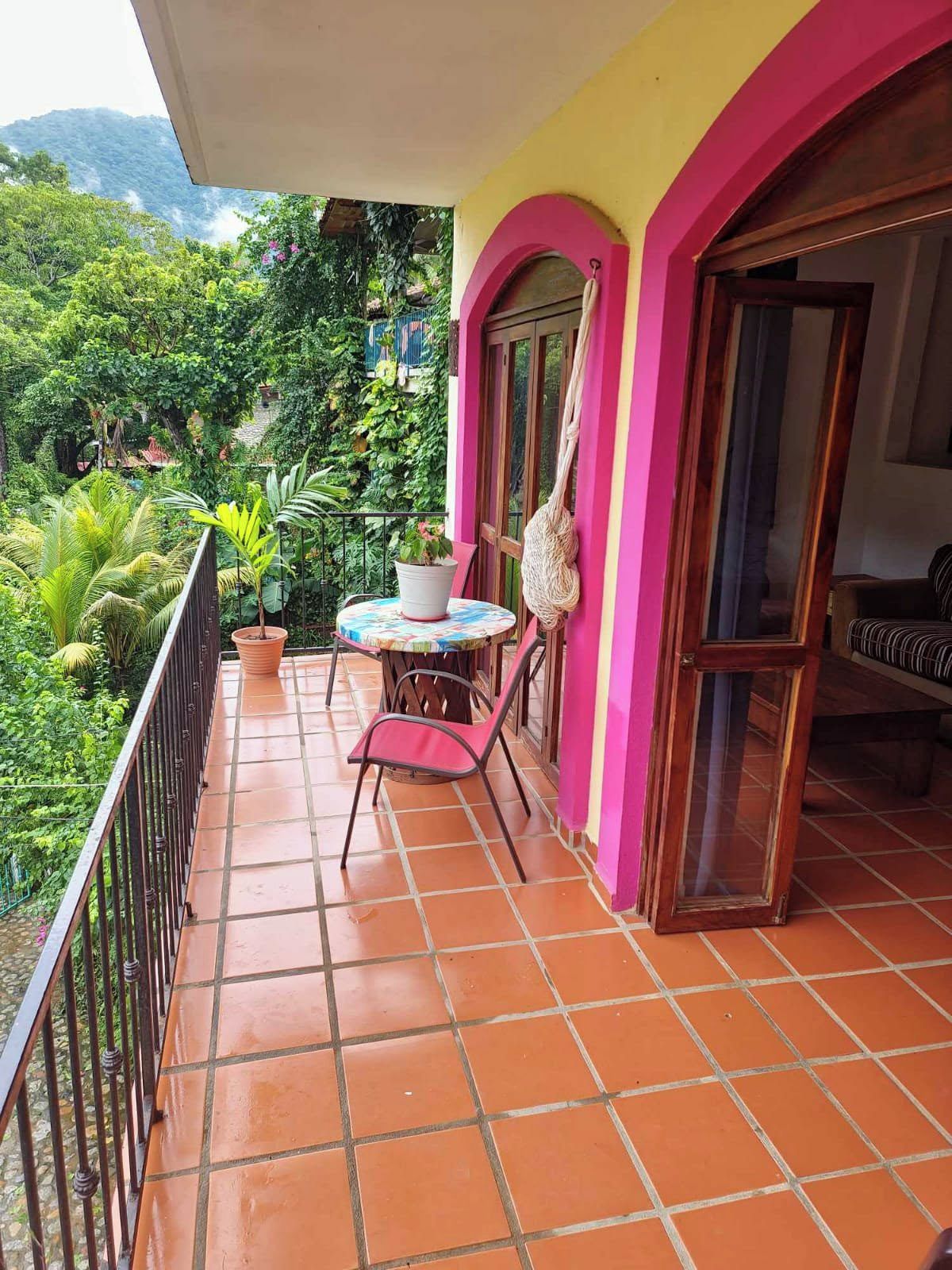 A balcony with a table and chairs, surrounded by a railing, and a view of lush greenery.