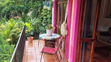 A balcony with a table and chairs, surrounded by a railing, and a view of lush greenery.