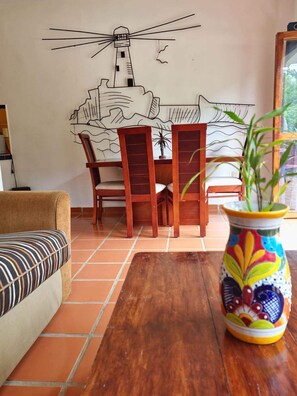 Uma sala de jantar com mesa e cadeiras de madeira, um vaso colorido e um mural na parede.