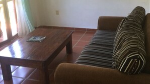 Een woonkamer met een houten tafel, een bank met gestreepte kussens en een raam met gordijnen.