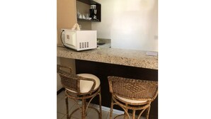 Eine Küchenzeile mit einer Kaffeemaschine, zwei Korbstühlen und einer Arbeitsplatte.