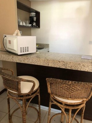 Eine Küchenzeile mit einer Kaffeemaschine, zwei Korbstühlen und einer Arbeitsplatte.
