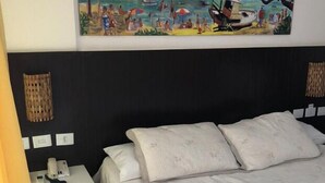 Ein Hotelzimmer mit Bett, Nachttisch, Telefon und einem Gemälde mit Strandmotiv an der Wand.