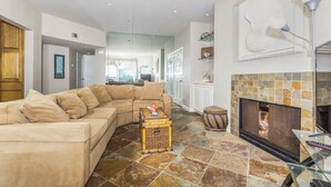 Una sala de estar con un sofá seccional color crema, una mesa de centro de vidrio y una chimenea con revestimiento de azulejos.