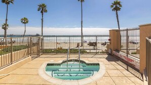 Zona de piscina con vista a la playa, rodeada de palmeras y una valla.