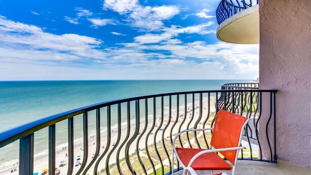 A balcony with a view of the beach and ocean.