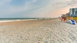 A beach with a sandy shore, a lifeguard tower, and buildings in the background.
