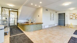 A hotel reception area with a reception desk, a glass door entrance, and a bulletin board on the wall.