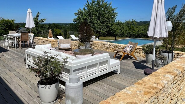 A wooden deck with outdoor furniture, a pool, and potted plants.