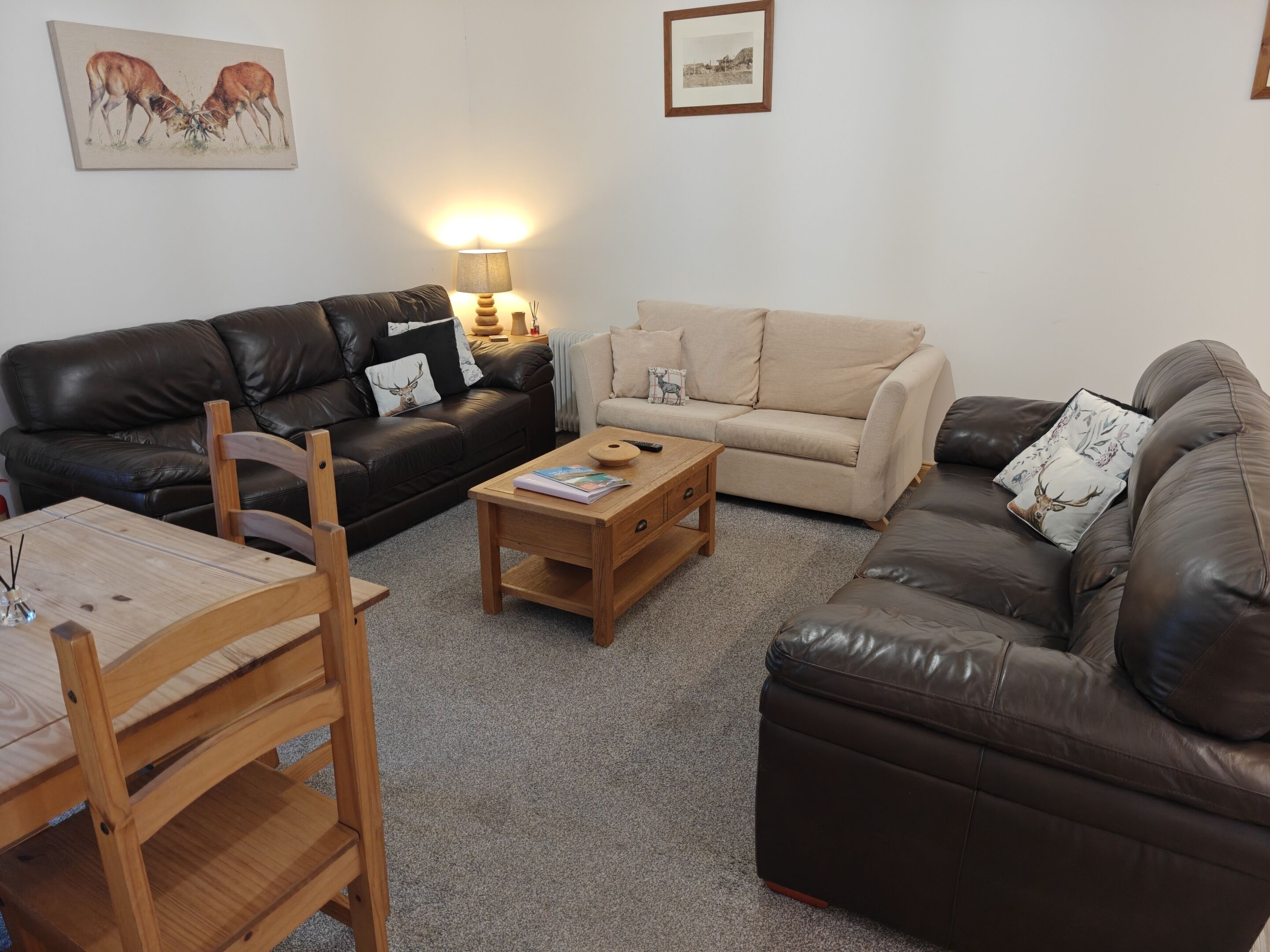 Ein Wohnzimmer mit einem schwarzen Ledersofa, einem beigen Sofa, einem Holztisch und einem Holzstuhl.