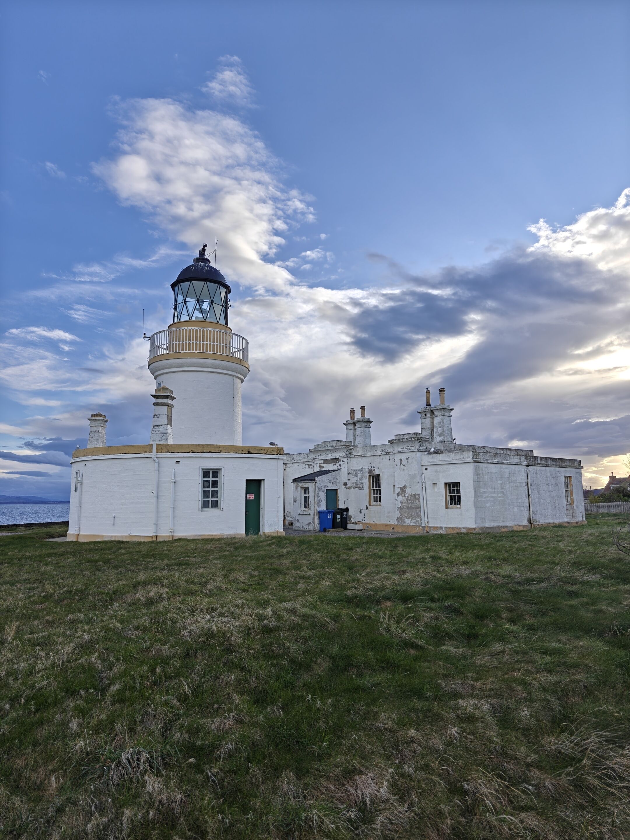 A lighthouse with a cylindrical tower and a smaller building with a green door.