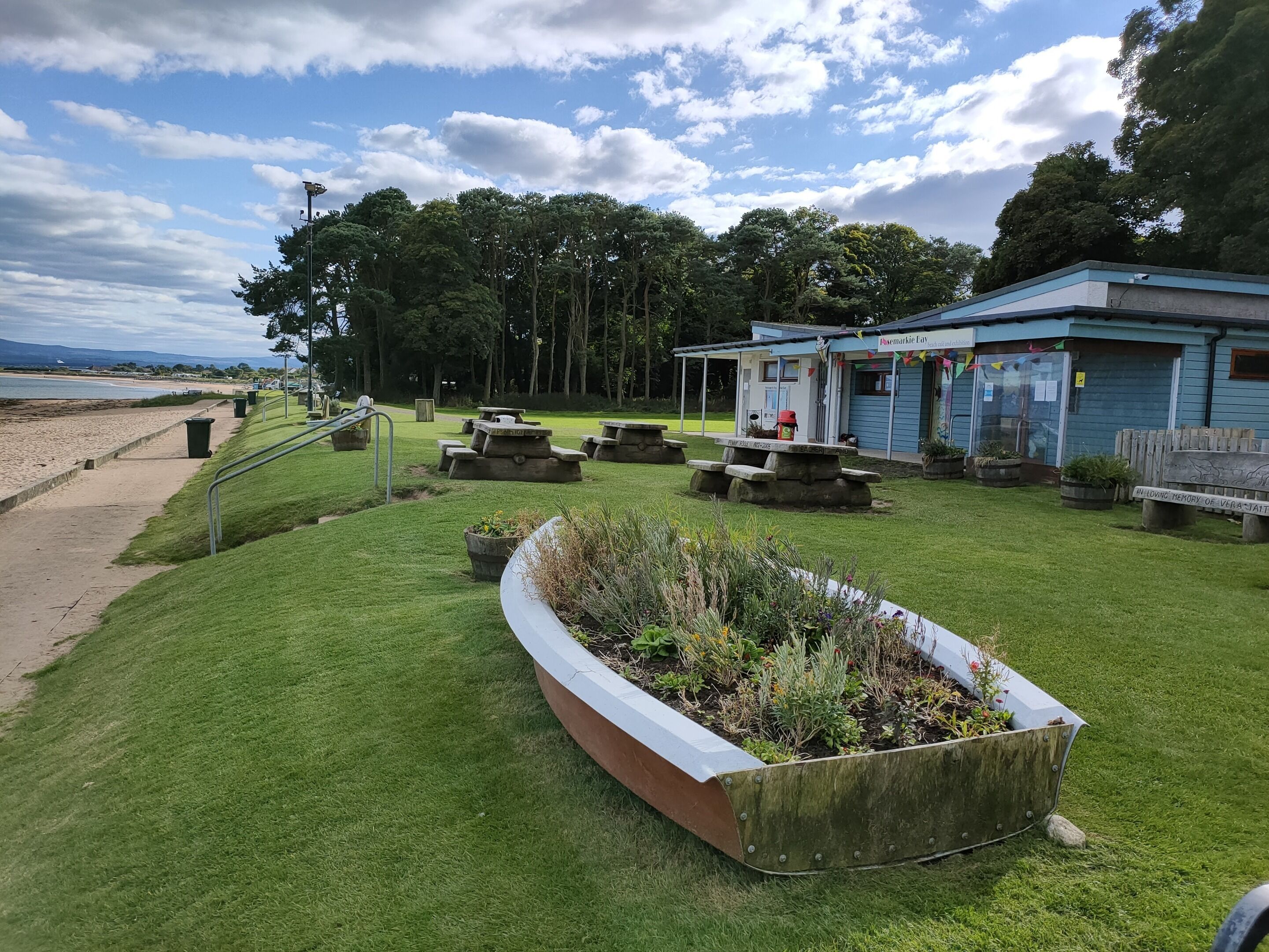 Un parc situé au bord de la plage, équipé de tables de pique-nique, d’un petit bâtiment et d’une zone herbeuse agrémentée d’un jardinière.