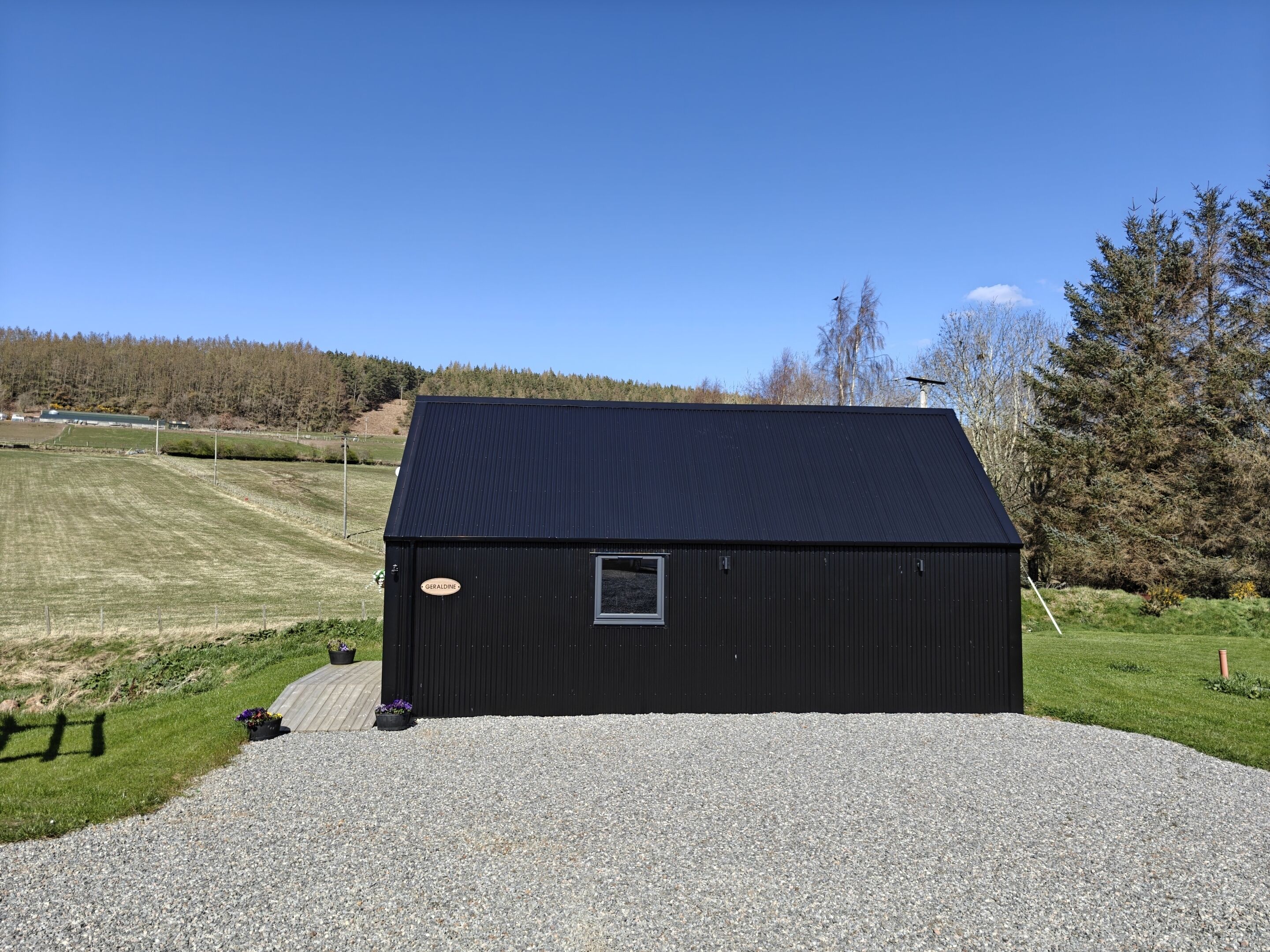 A black metal building with a gravel driveway and a small window.
