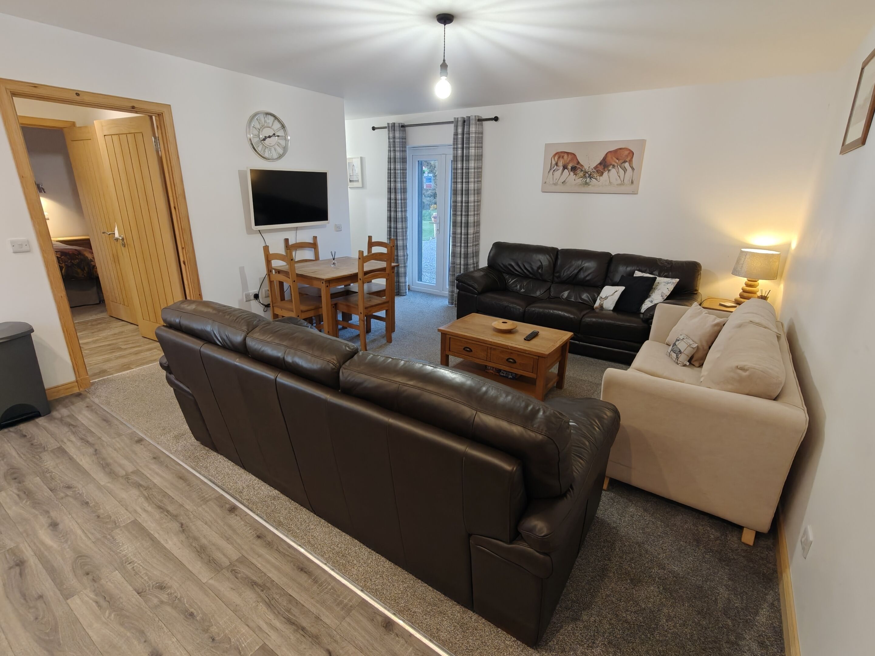 A living room with a brown leather sofa, a black leather couch, a wooden coffee table, a TV, and a dining area with a wooden table and chairs.