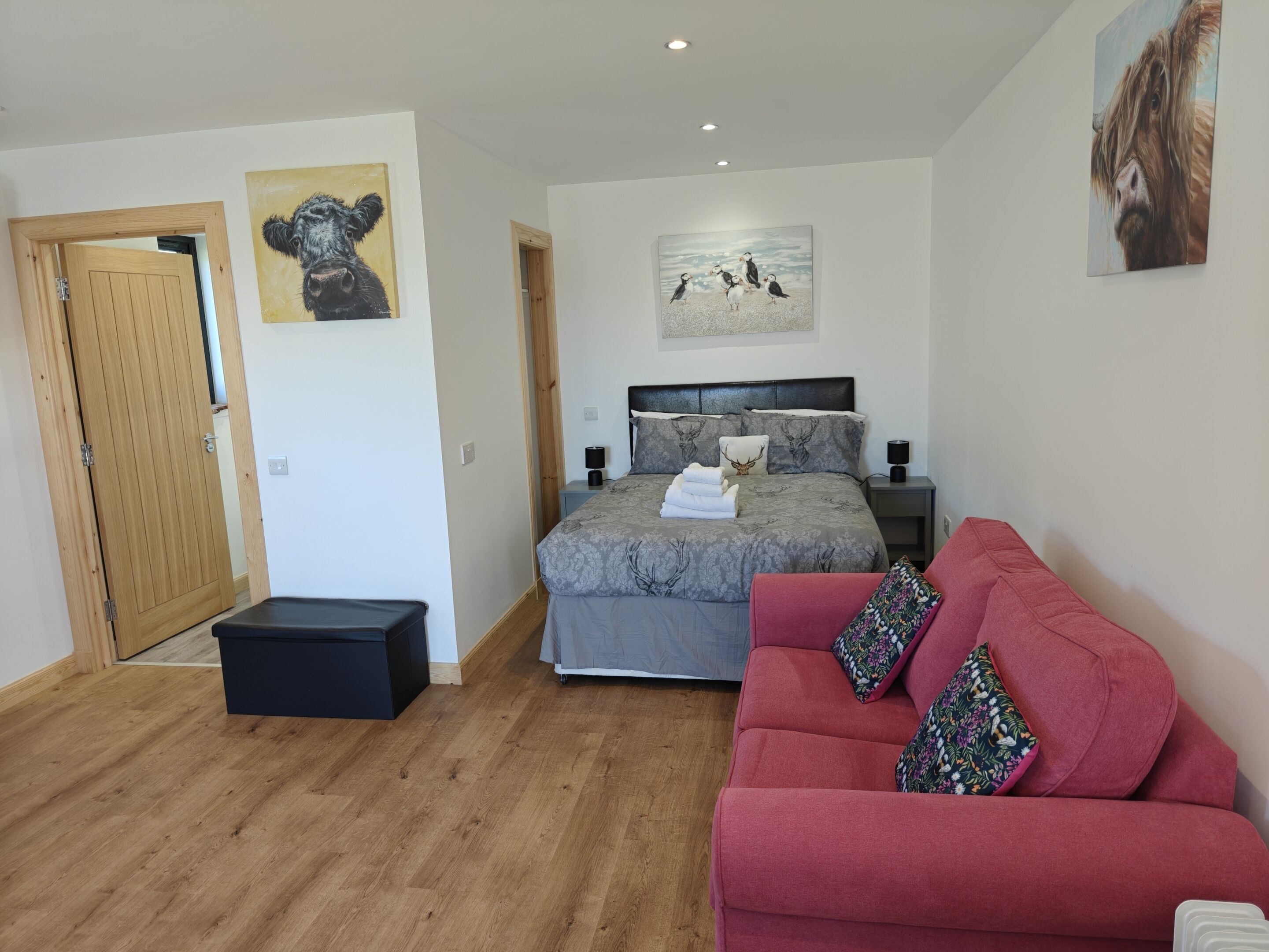 A bedroom with a bed, a red sofa, a wooden floor, and artwork on the walls.