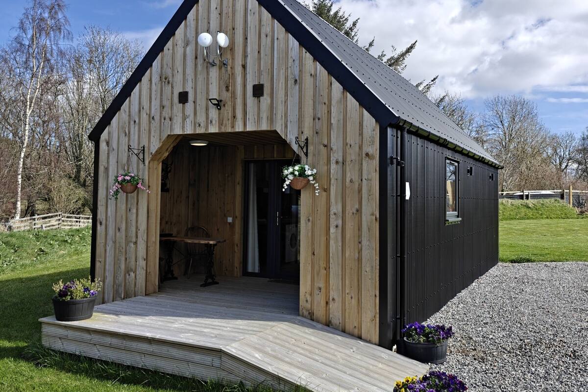 A wooden barn-style building with a sloped roof, a porch, and a gravel driveway.