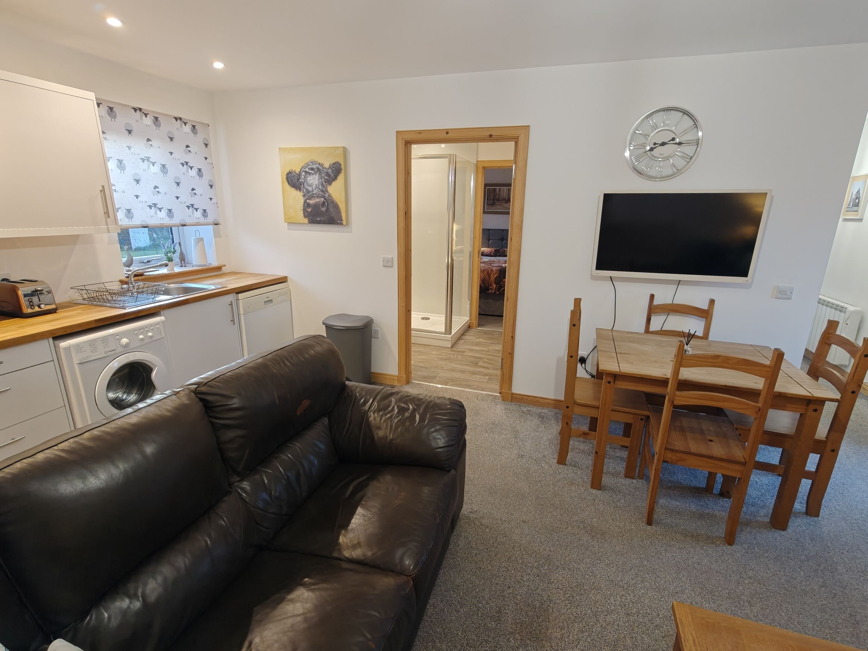 A compact living space with a kitchenette, a sofa, a dining table with chairs, and a TV.