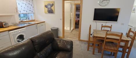 A compact living space with a kitchenette, a sofa, a dining table with chairs, and a TV.