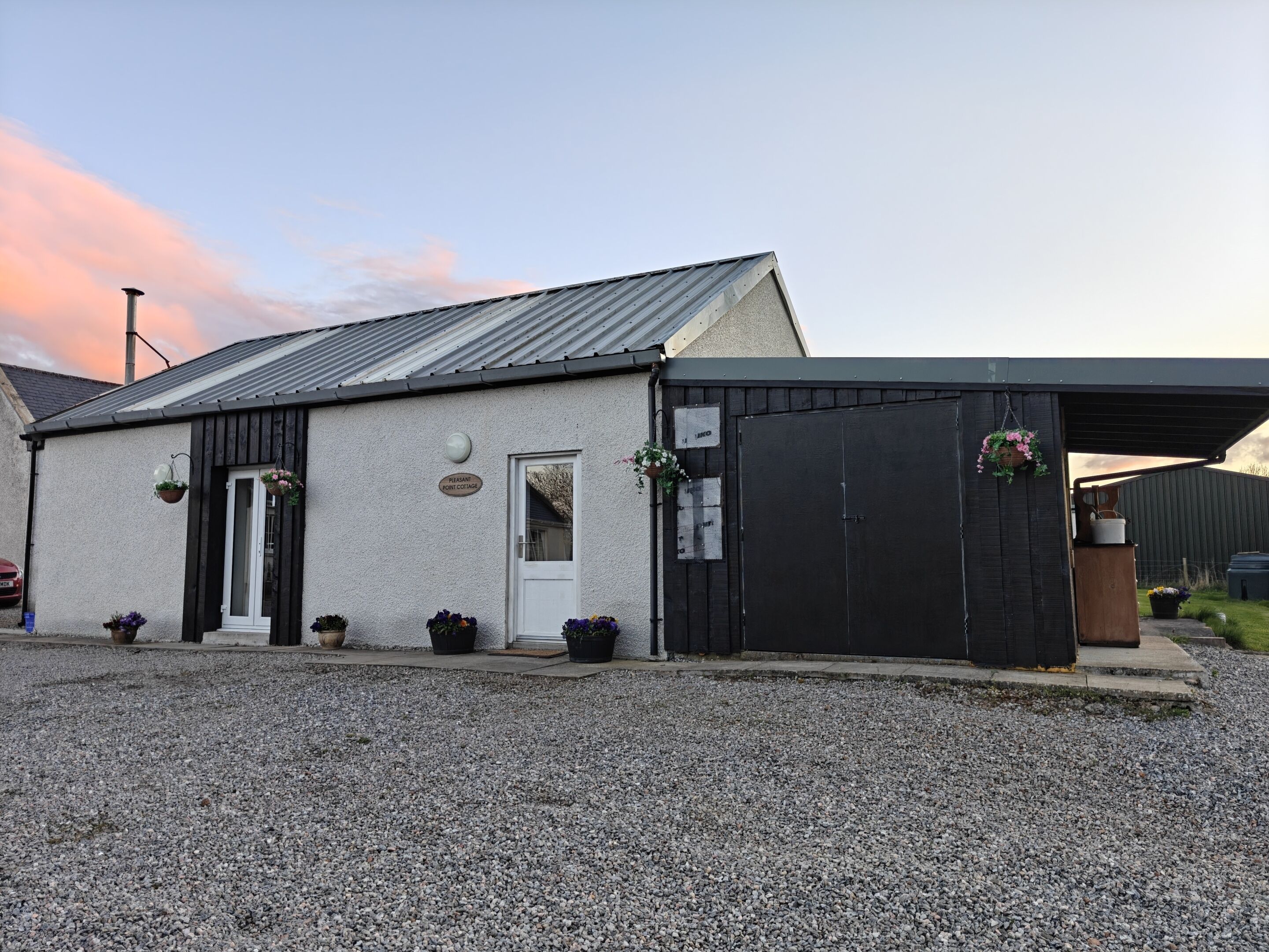 A small building with a white door and a black garage door, surrounded by gravel.