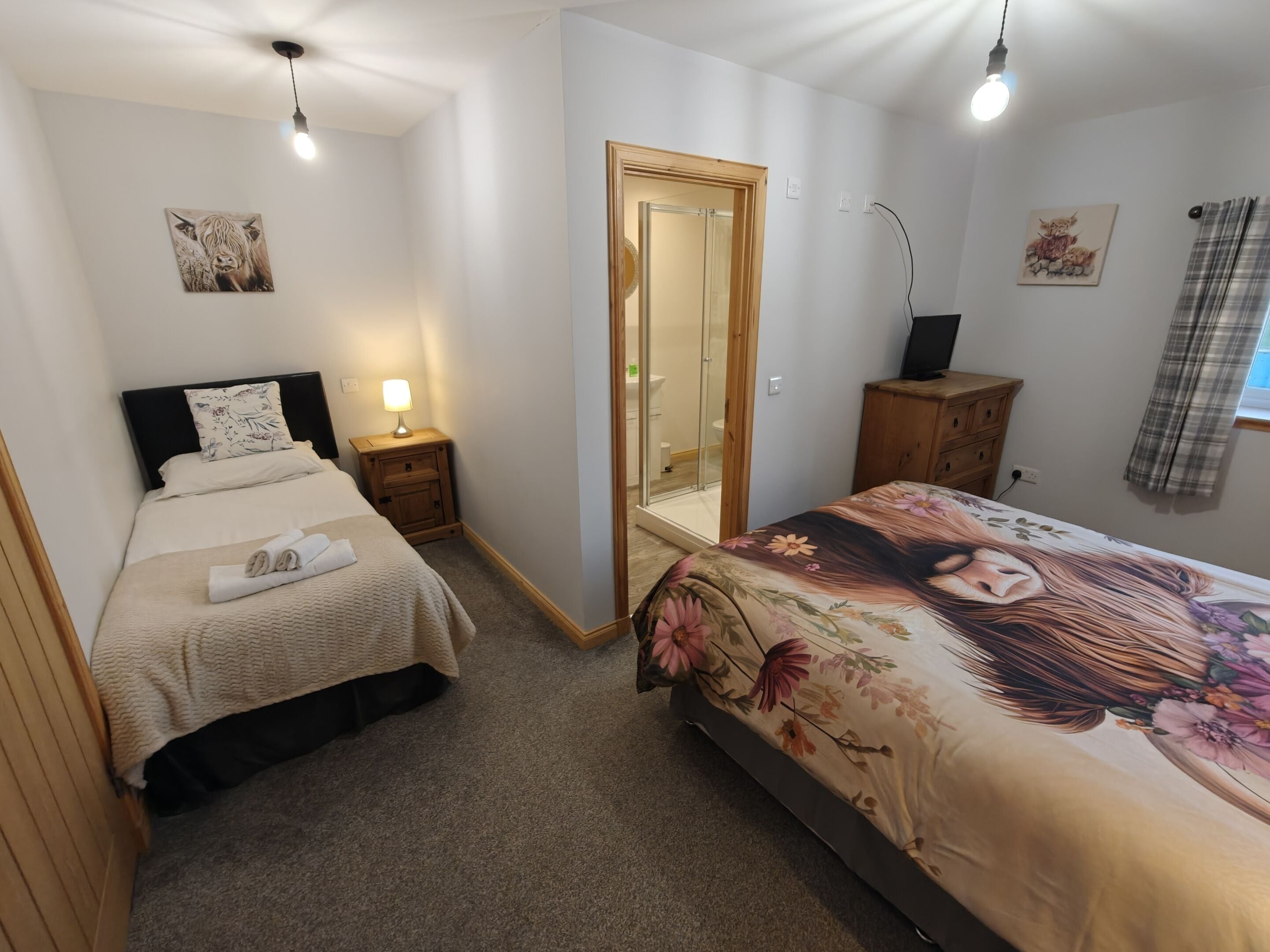 A bedroom with two beds, a wooden wardrobe, a bedside table with a lamp, a mirror, and a painting on the wall.