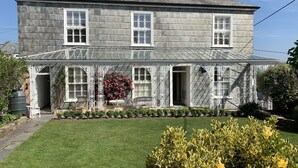 Une maison en pierre à deux étages, dotée d’un porche abrité, d’une grande fenêtre et d’un jardin agrémenté d’un élément décoratif aquatique.