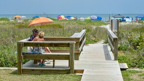 Een houten looppad dat leidt naar strandparasols en een strandgedeelte.