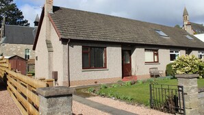 A single-story house with a sloped roof, a visible chimney, and a small front porch with a bench. - Newholme Self-catering Bungalow (Pitlochry)