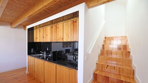 Une cuisine moderne avec des meubles en bois et un plan de travail noir, un escalier en bois et un mur blanc.