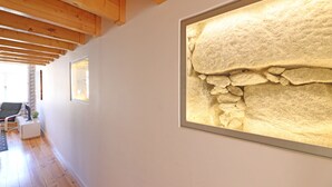Un couloir avec des poutres en bois, une grande œuvre d’art encadrée représentant une surface texturée, et un coin salon avec un fauteuil et une petite table.