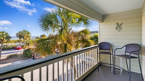 A balcony with a railing, two chairs, and a view of palm trees and a road.