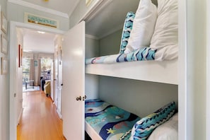 A bunk bed with a nautical-themed bedspread, a hallway leading to a living area, and a door with a sign above it. - Beachfront well stocked 1 bedroom sea cabin w/ beach view, pier, community pool. (Isle of Palms)