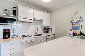 A kitchen with white cabinets, a microwave, a coffee maker, and a sink. - Beachfront well stocked 1 bedroom sea cabin w/ beach view, pier, community pool. (Isle of Palms)