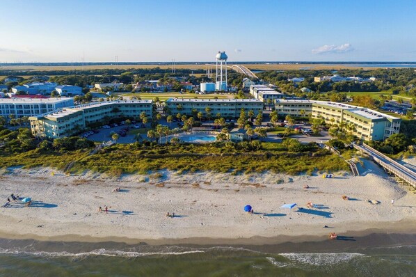 Un hôtel situé sur la côte, composé de plusieurs bâtiments, avec une plage et un château d’eau.