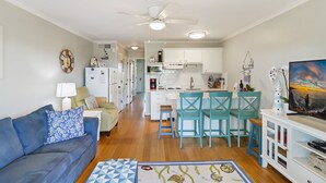 A compact living space with a kitchenette, a dining area with chairs, a sofa with a patterned cushion, and a ceiling fan.