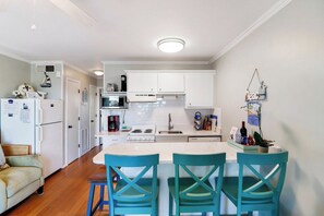 Une cuisine compacte avec des meubles blancs, un îlot central et des chaises de couleur turquoise.