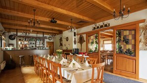 Un comedor con mesas y sillas de madera, una barra con estantes llenos de botellas y una araña.