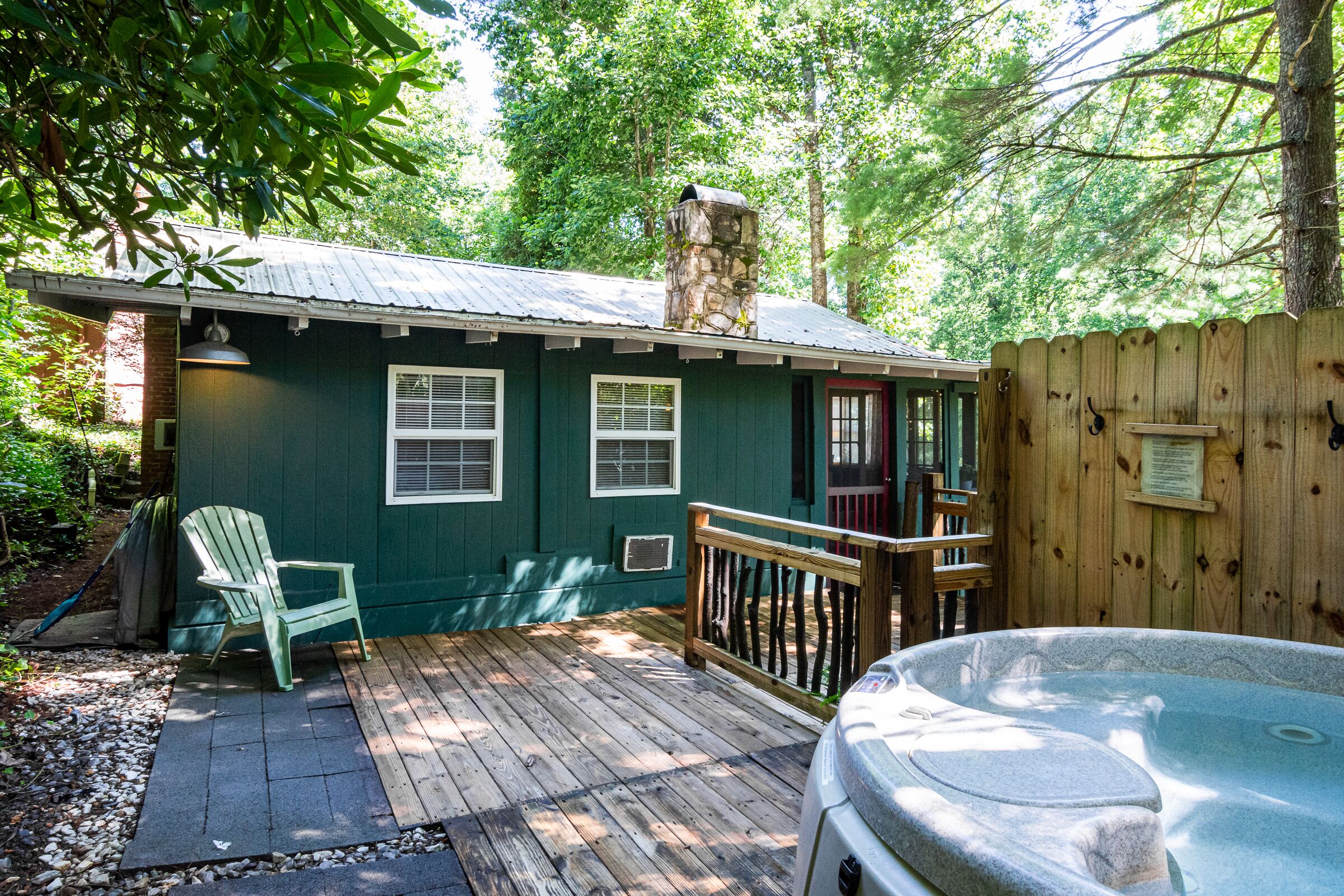A cozy cabin with a hot tub, wooden deck, and a stone chimney.