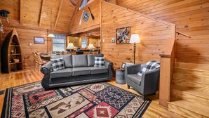 L'intérieur d'un chalet confortable, avec des murs en bois, un canapé gris foncé, un fauteuil assorti et un tapis à motifs.
