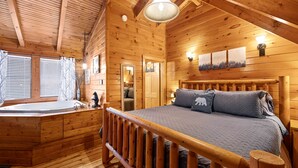 Une chambre située dans une cabane en rondins, avec un lit en bois, une grande fenêtre, une baignoire intégrée et des murs en bois.