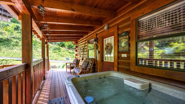 Une terrasse en bois avec un jacuzzi, des chaises et une vue sur la verdure environnante.
